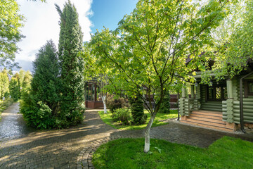Picturesque summer landscape. The sun's rays fall on the paved paths and lawn near a wooden house made of logs.