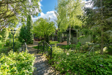 Fabulous summer landscape against the blue sky. A small bridge with wrought-iron railings, a log house behind the trees.