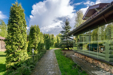 The wonderful beauty of the landscape on the territory of the house with a glazed terrace. White clouds on a blue sky on a sunny summer day.