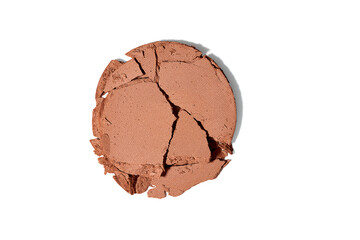A broken compact powder in a warm, neutral shade, scattered into various cracked pieces.