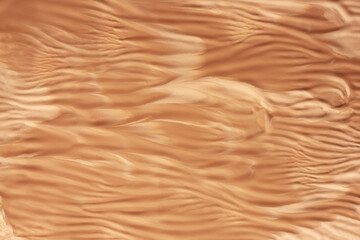 Textured surface in a warm beige-brown tone, resembling the ripples of sand dunes or background of cosmetic product