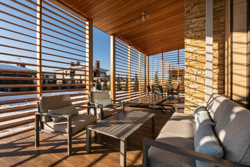 A stylish outdoor lounge area features comfortable seating and wooden slats, providing a perfect view of the snowy mountains on a sunny winter day.