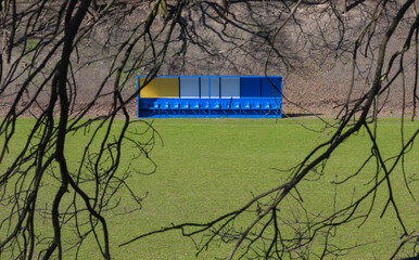 Blue and Yellow Team Bench on a Soccer Field, Framed by Tree Branches © Elninho
