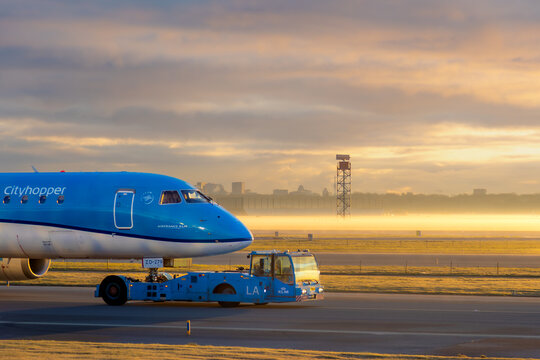 Sunrise silhouette of KLM Cityhopper Embraer jet towed with pushback truck in from of Amsterdam Skyline