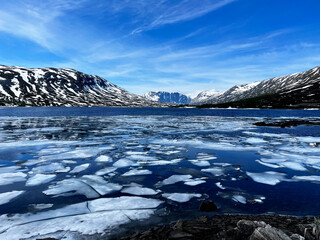 Scenic view of a frozen lake with ice floes in the foreground and a black, snow-covered mountain...