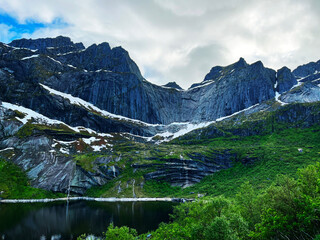 View on a mountain wall behind a lake with small waterfalls and snow embedded in a green scenery