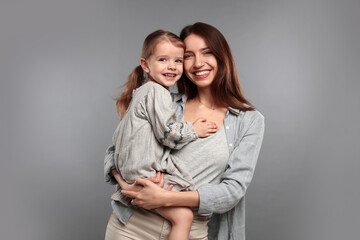 Portrait of happy mother with her cute little daughter on grey background
