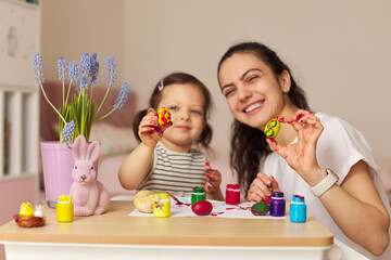 Happy mother and cute little child girl showing painted Easter egg at home. Mom and daughter...