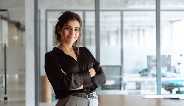 Portrait of successful middle eastern young business woman with crossed arms smiling confident at camera. Latina or indian female manager leader specialist businesswoman standing in office. Copy space