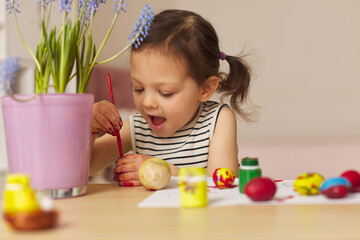 Little child girl paint Easter eggs at home. kid is preparing for Easter.
