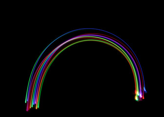 A long exposure photograph of colourful lights in a rainbow arc shape against a black background