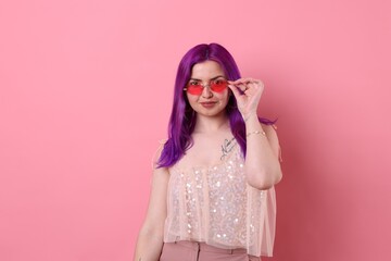 Beautiful woman with bright purple hair and tattoo in Latin on pink background