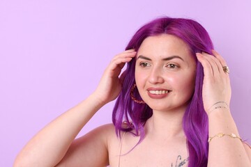Obraz premium Beautiful woman with bright purple hair and tattoo on lilac background. Space for text