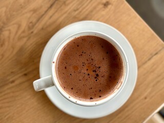 Flat lay portrait of rich hot chocolate served in a clear white cup, elegantly placed on a wooden table – a cozy and indulgent treat. Cisauk, Indonesia - March 14, 2025