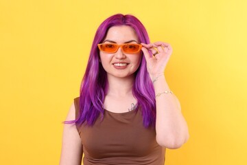 Beautiful woman with bright purple hair on yellow background