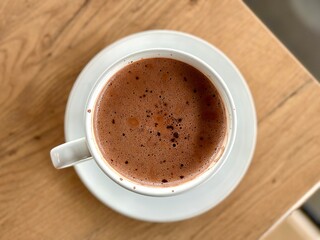 Flat lay portrait of rich hot chocolate served in a clear white cup, elegantly placed on a wooden table – a cozy and indulgent treat. Cisauk, Indonesia - March 14, 2025