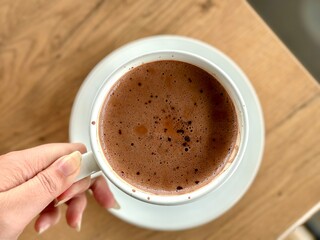 Flat lay portrait of rich hot chocolate served in a clear white cup, elegantly placed on a wooden table – a cozy and indulgent treat. Cisauk, Indonesia - March 14, 2025