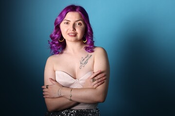 Fototapeta premium Beautiful woman with bright purple hair and tattoo in Latin on light blue background