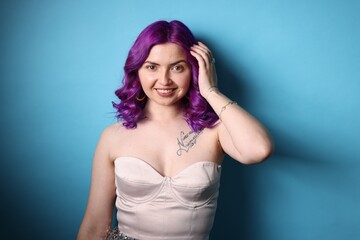 Obraz premium Beautiful woman with bright purple hair and tattoo in Latin on light blue background