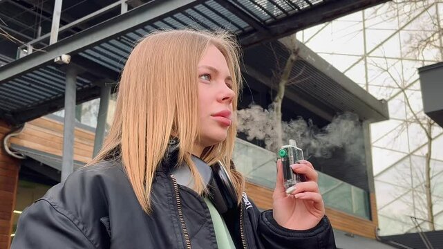 Young woman smokes disposable vape outside	