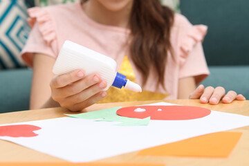 Girl applying glue onto paper figure for her creative project at table indoors, closeup. Art and...