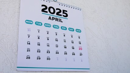 A man tears off a March page of a wall calendar 2025 to reveal the next one with the marked Easter date