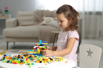 Cute girl playing with building blocks at white table indoors