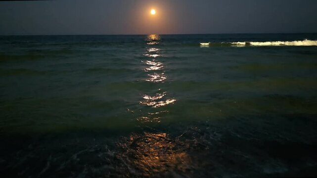 Pleine lune sur la Mer Noire en ao&ucirc;t. S'&eacute;levant au-dessus de l'horizon, la lune illumine les vagues du littoral, cr&eacute;ant une tra&icirc;n&eacute;e dor&eacute;e ondulante &agrave; la surface de la mer.