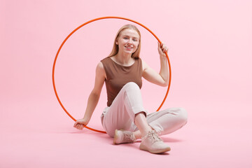 Beautiful young woman with hula hoop on pink background