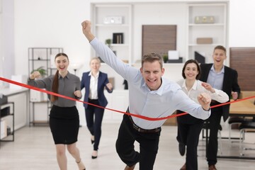 Fototapeta premium Competition concept. Happy businessman crossing red finish line ahead of his colleagues in office