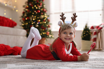 Little girl in Christmas costume with candy cane lying on floor at home