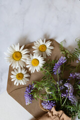 Fototapeta premium Florist at work: a pretty woman prepares a summer bouquet of white gypsophila on a gray desk. Kraft paper, scissors, greeting envelope on the table. View from above. The composition is flat.