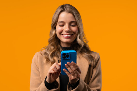 Pretty Woman Surfing Internet On Smartphone.girl With Smile On Yellow Background