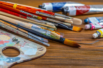 Old used brushes and paint tubes in an artist's studio, palette with multi-colored spots of oil or...