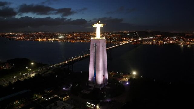Night Scape Of Christ The King At Lisbon In Lisbon District Portugal. Illuminated King Christ. 25 Of April Bridge. Christ The King At Lisbon In Portugal. Tejo River Coast. Landmark Sanctuary.