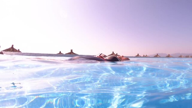 Close-up of an adult woman's body floating peacefully in waters of a pool at resort, blue tiled walls, relaxing in swimming pool on sunny vacation day