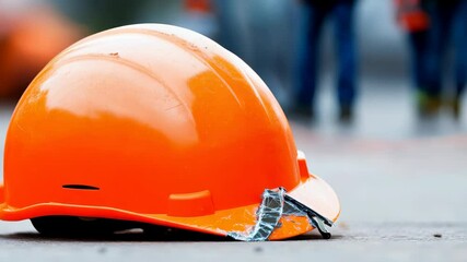 Close-up of a bright orange construction helmet resting on the ground at an outdoor work site, emphasizing safety and protection in the construction industry.