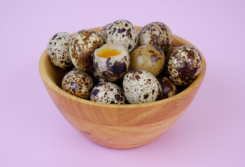 Raw quail eggs in wooden bowl on pink	