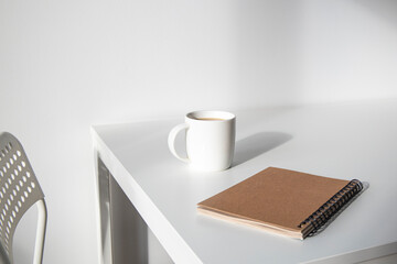 Notepad, white cup with coffee on a white table