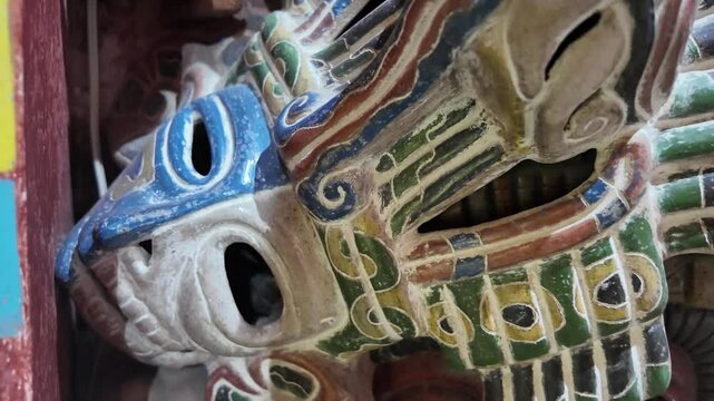 A mask with a green and blue design. The mask is made of wood and has a hole in the middle