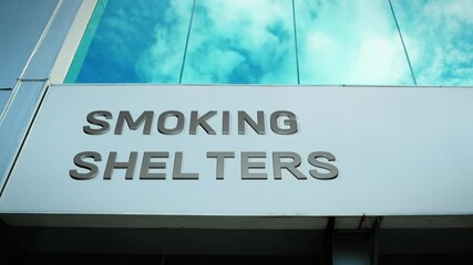 Smoking shelter sign on a modern building with a reflection of the sky on glass windows, symbolizing public space, safety, and designated areas