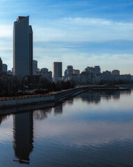 Fototapeta premium Cityscape with river and buildings reflected, panoramic view. Silhouettes of buildings are visible against the sky. Ukrainian city of Dnepr