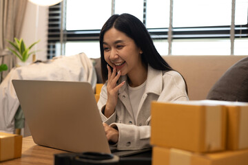 A woman is holding two boxes and smiling. She is sitting in front of a laptop. The boxes are brown and appear to be gifts. The woman seems happy and excited about the boxes

