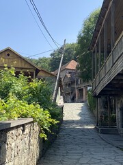 Narrow cobblestone street leads through old village with traditional wooden houses featuring sloped roofs and stone walls     