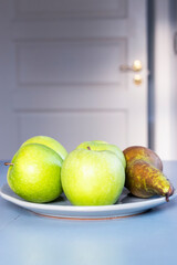 green apples and a pear on a plate on kitchen table