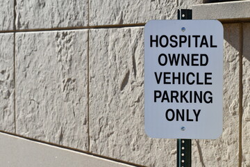 Fototapeta premium Hospital Owned Vehicle Parking Only sign. Brick wall in background.