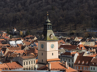 Fototapeta premium a detailed, elevated view of the Council Tower (Turnul Sfatului) in Brașov, Romania, set amidst the city's characteristic terracotta rooftops and against a backdrop of a forested mountain.