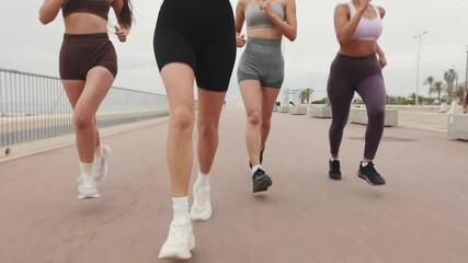 Four diverse women enjoy a fitness run together on a beachside path. They are smiling, wearing sportswear, and running towards the camera. - Powered by Adobe