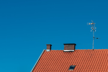 Red Tiled Roof with Chimneys and TV Antenna Against a Clear Blue Sky