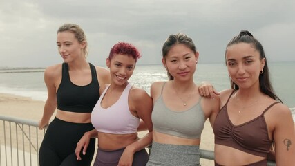 Four diverse female friends stand by a beach railing, radiating health and wellness. Their fitness wear and smiles evoke a sense of community and body positivity.